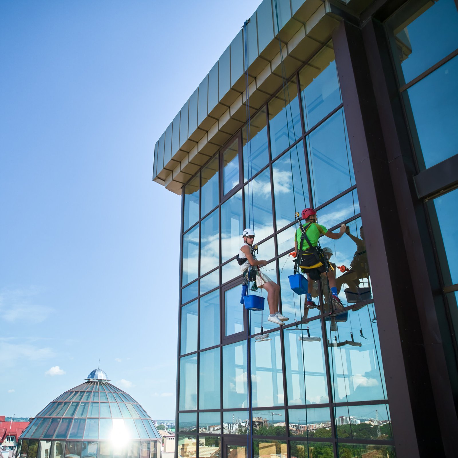 Über uns industrial mountaineering worker cleaning window outside building.